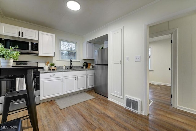 kitchen with ornamental molding, white cabinetry, light hardwood / wood-style flooring, and stainless steel appliances