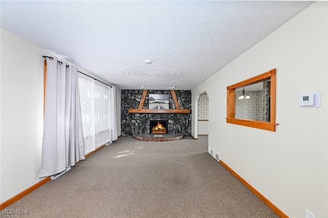 unfurnished living room featuring carpet flooring, a stone fireplace, and a textured ceiling