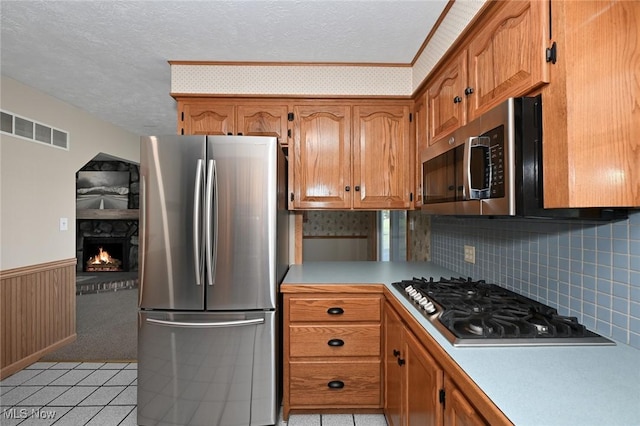 kitchen featuring a fireplace, light tile patterned floors, stainless steel appliances, and a textured ceiling