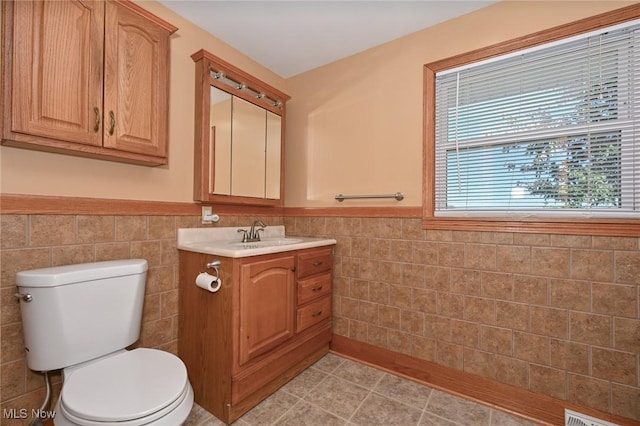 bathroom with vanity, toilet, and tile walls