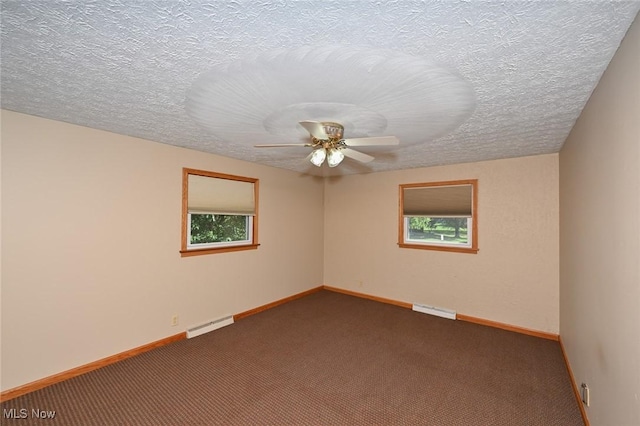 empty room with a wealth of natural light, a textured ceiling, dark carpet, and ceiling fan