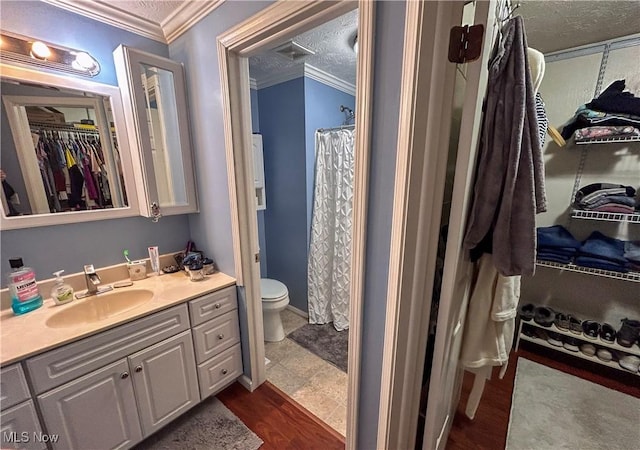 bathroom with toilet, wood-type flooring, a textured ceiling, ornamental molding, and vanity