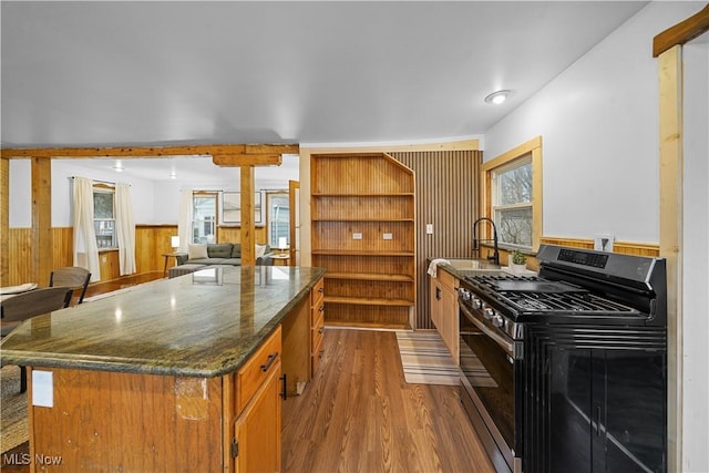 kitchen featuring sink, wooden walls, dark stone countertops, gas range oven, and wood-type flooring