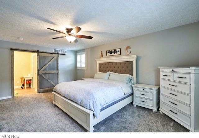 carpeted bedroom with ceiling fan, a barn door, and a textured ceiling