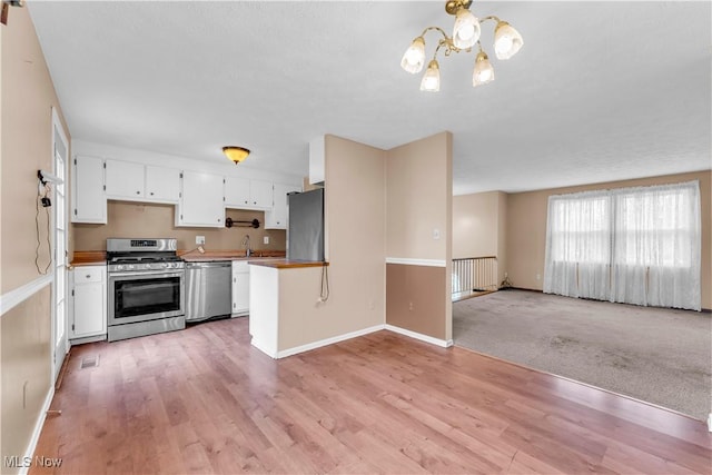 kitchen featuring light wood-type flooring, stainless steel appliances, pendant lighting, an inviting chandelier, and white cabinets