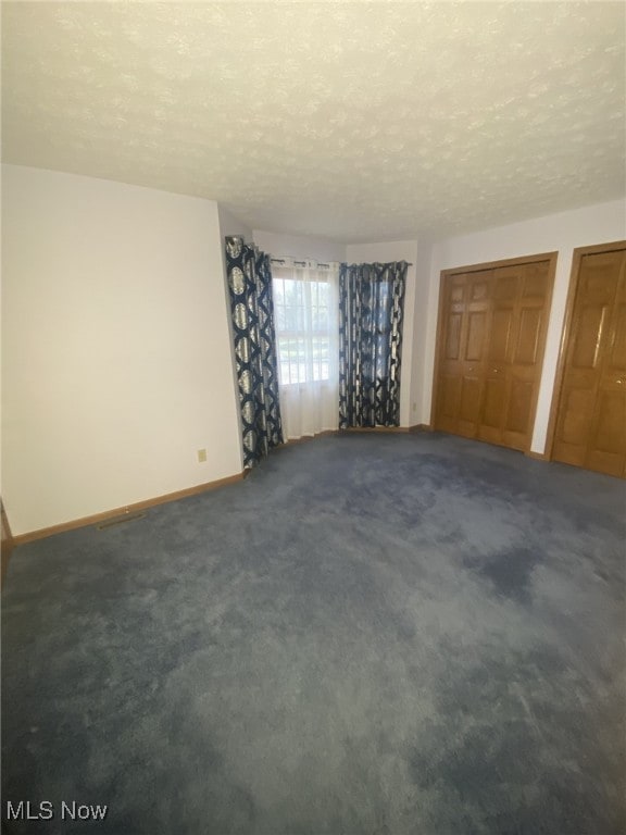 unfurnished bedroom featuring dark carpet and a textured ceiling