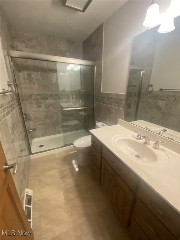 bathroom featuring tile patterned floors, toilet, a shower with door, and tile walls