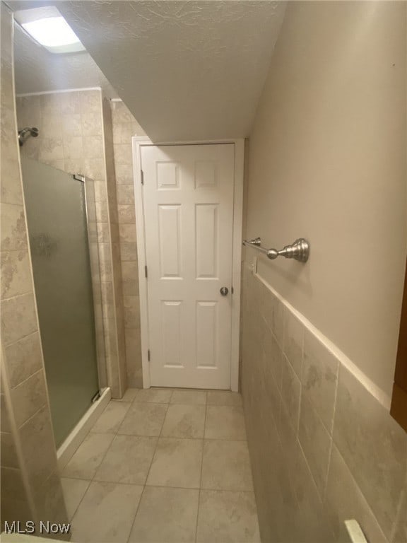 bathroom featuring tile patterned flooring, a textured ceiling, a shower with door, and tile walls