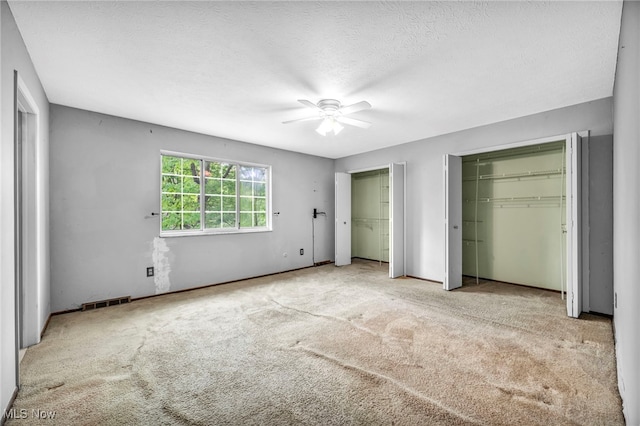 unfurnished bedroom with a textured ceiling, ceiling fan, light carpet, and multiple closets