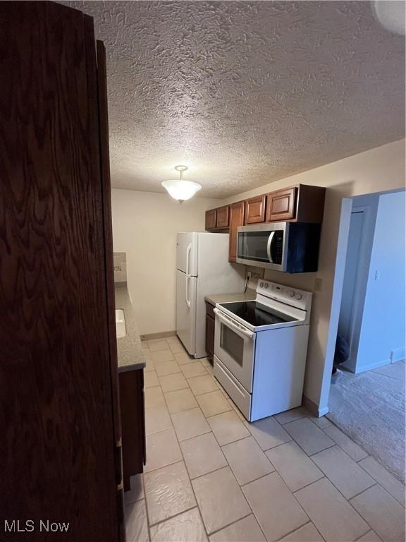 kitchen featuring a textured ceiling, light tile patterned floors, and white appliances