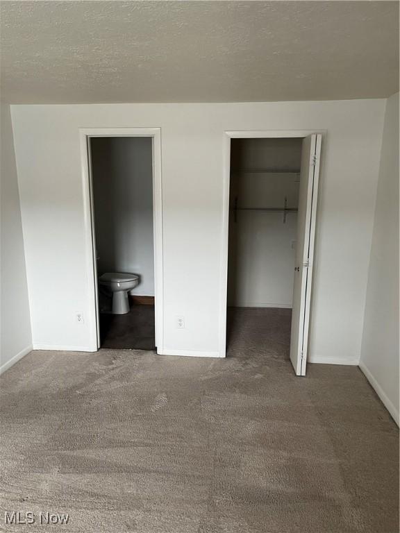 unfurnished bedroom featuring ensuite bathroom, dark carpet, a textured ceiling, a spacious closet, and a closet