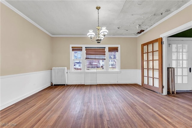 unfurnished dining area with radiator, crown molding, a notable chandelier, and hardwood / wood-style flooring