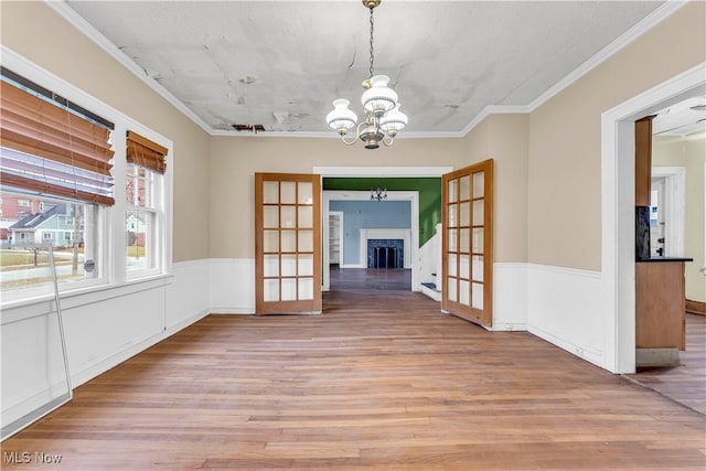 unfurnished dining area featuring french doors, an inviting chandelier, ornamental molding, and light wood-type flooring