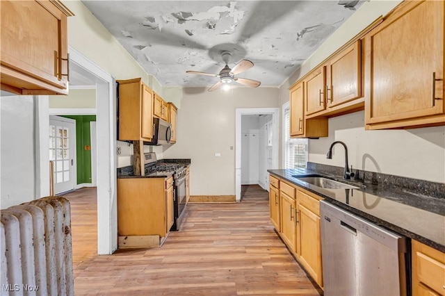 kitchen with appliances with stainless steel finishes, light hardwood / wood-style floors, dark stone counters, and sink