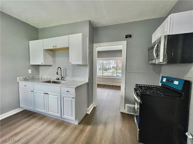 kitchen featuring white cabinetry, sink, black range, and light hardwood / wood-style floors