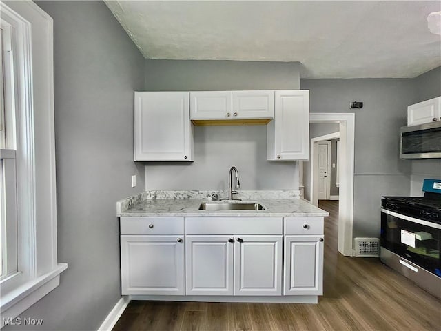 kitchen with sink, hardwood / wood-style flooring, appliances with stainless steel finishes, light stone counters, and white cabinetry