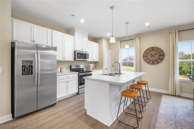 kitchen featuring white cabinets, stainless steel appliances, hanging light fixtures, and a center island with sink