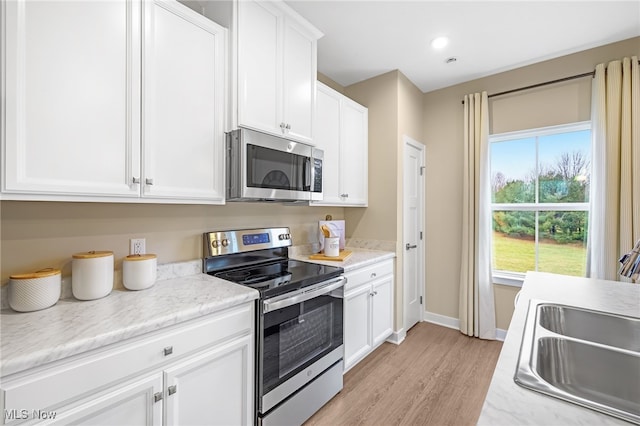 kitchen with white cabinets, sink, light wood-type flooring, light stone counters, and stainless steel appliances