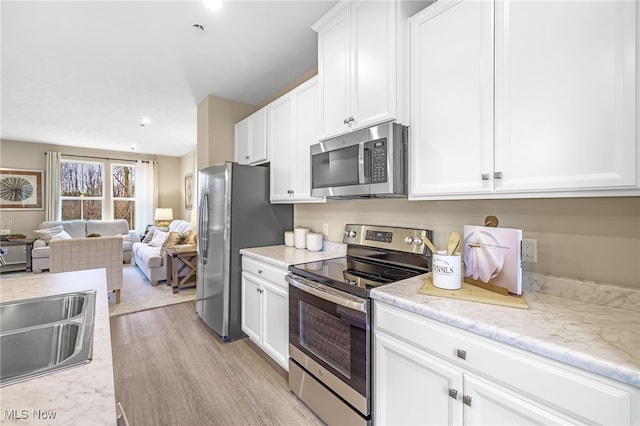 kitchen with white cabinetry, sink, light stone counters, light hardwood / wood-style flooring, and appliances with stainless steel finishes