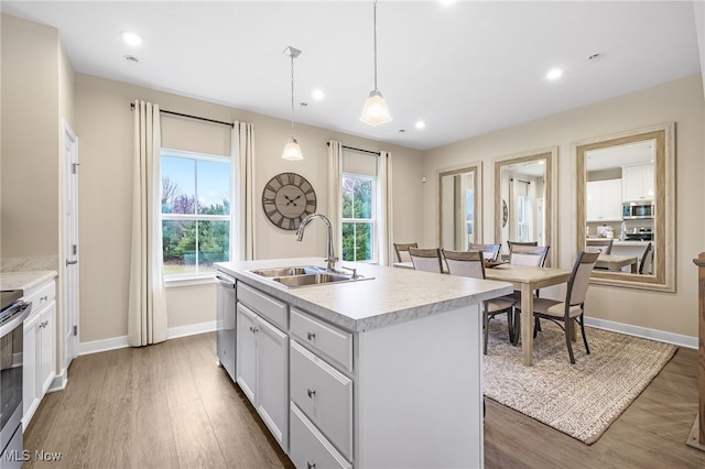 kitchen with appliances with stainless steel finishes, a kitchen island with sink, sink, white cabinetry, and hanging light fixtures