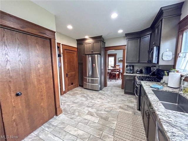 kitchen with light stone countertops, appliances with stainless steel finishes, dark brown cabinets, and sink