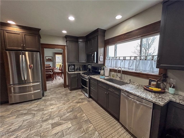 kitchen with light stone countertops, appliances with stainless steel finishes, dark brown cabinetry, and sink