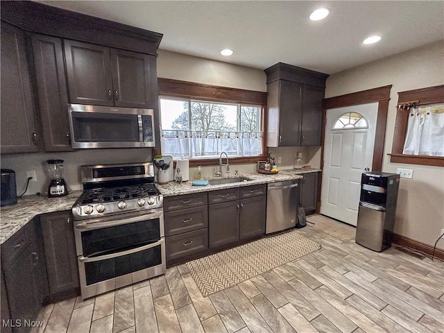 kitchen featuring dark brown cabinets, sink, light stone countertops, and stainless steel appliances