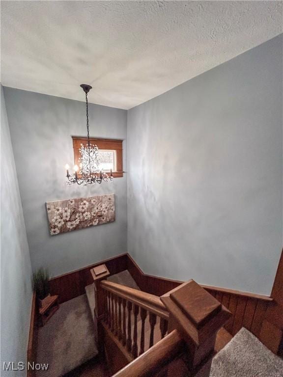 staircase with carpet flooring, a notable chandelier, and a textured ceiling