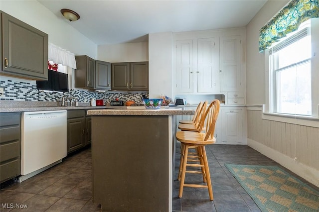 kitchen featuring a breakfast bar, a center island, white dishwasher, dark tile patterned floors, and tasteful backsplash