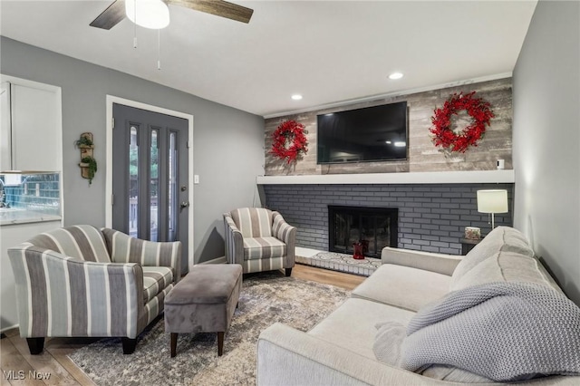 living room with a brick fireplace, ceiling fan, and light hardwood / wood-style flooring