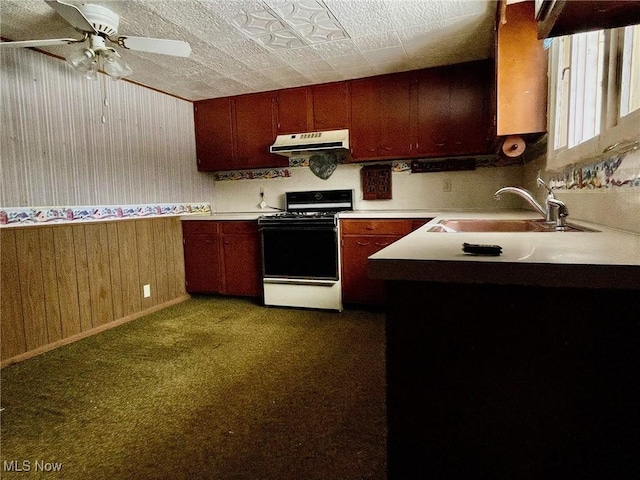 kitchen featuring ceiling fan, sink, dark colored carpet, stove, and wooden walls