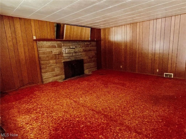 unfurnished living room with a fireplace, carpet, and wood walls