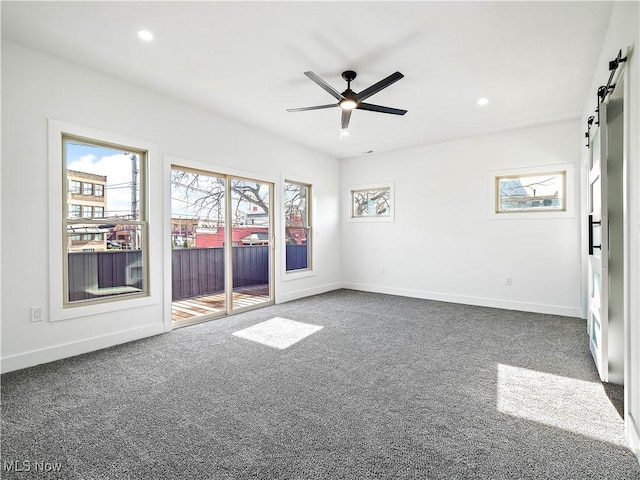 carpeted empty room with a barn door and ceiling fan