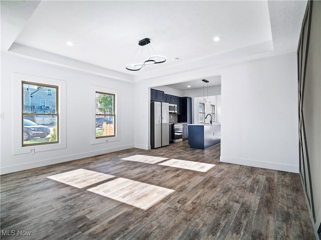 unfurnished living room with a raised ceiling, a chandelier, sink, and dark wood-type flooring