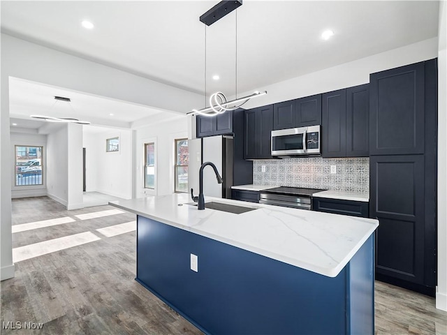 kitchen with appliances with stainless steel finishes, light stone counters, sink, a center island with sink, and decorative light fixtures