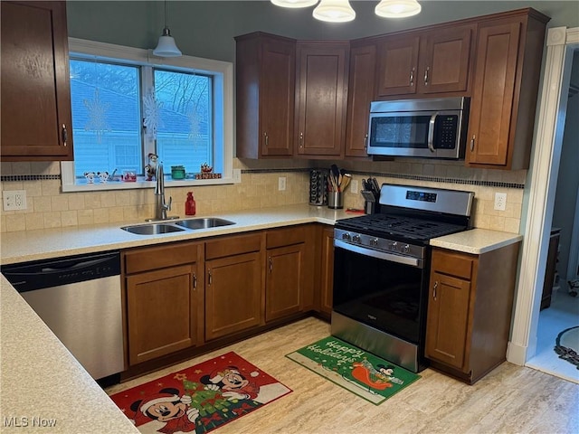 kitchen featuring appliances with stainless steel finishes, backsplash, sink, decorative light fixtures, and light hardwood / wood-style flooring