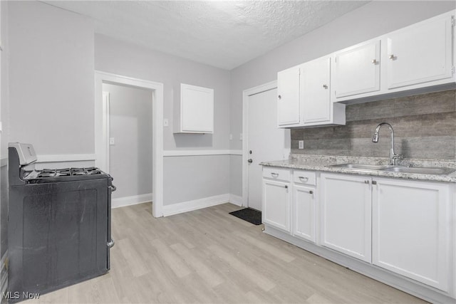 kitchen featuring sink, light hardwood / wood-style flooring, stove, a textured ceiling, and white cabinets