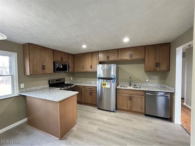 kitchen featuring sink, light hardwood / wood-style flooring, a textured ceiling, appliances with stainless steel finishes, and kitchen peninsula