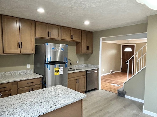 kitchen featuring light stone counters, sink, light wood-type flooring, and appliances with stainless steel finishes