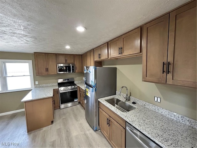 kitchen featuring light stone countertops, appliances with stainless steel finishes, a textured ceiling, sink, and light hardwood / wood-style flooring