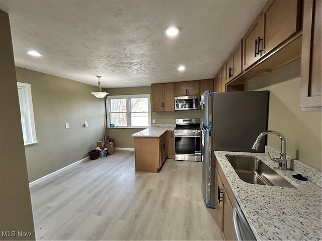 kitchen with light stone countertops, appliances with stainless steel finishes, sink, pendant lighting, and light hardwood / wood-style floors