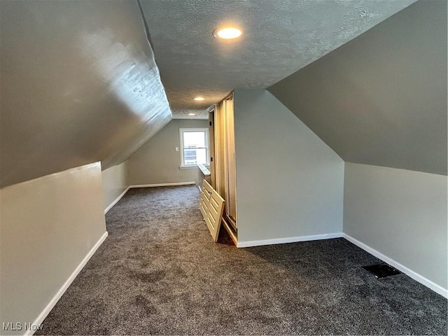 additional living space with vaulted ceiling, dark carpet, and a textured ceiling