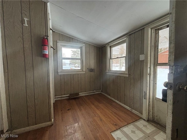 spare room with light wood-type flooring, wooden walls, and vaulted ceiling