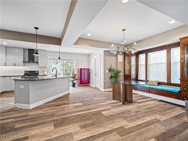 kitchen with stainless steel range oven, hanging light fixtures, tasteful backsplash, and an island with sink