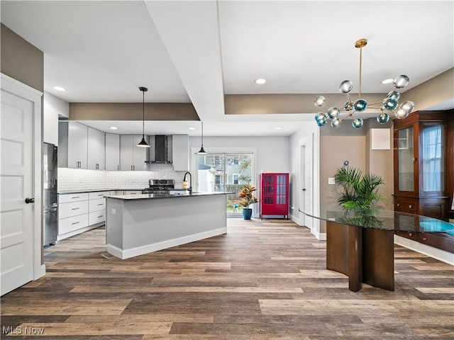 kitchen with appliances with stainless steel finishes, backsplash, wall chimney exhaust hood, decorative light fixtures, and a center island with sink