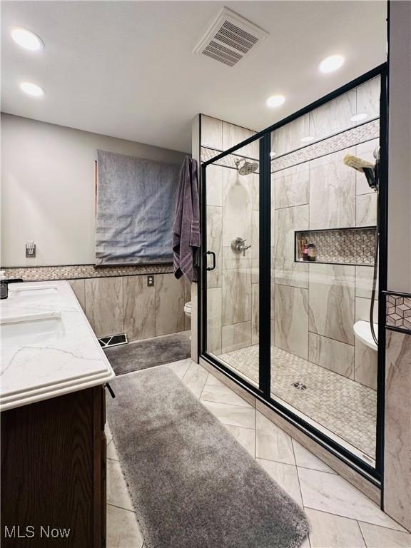 bathroom featuring vanity, toilet, a shower with shower door, and tile walls