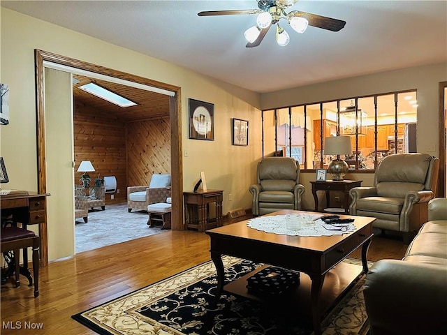 living room with hardwood / wood-style flooring, lofted ceiling with skylight, ceiling fan, and wooden walls