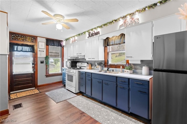 kitchen featuring white cabinets, sink, blue cabinetry, gas range gas stove, and stainless steel refrigerator