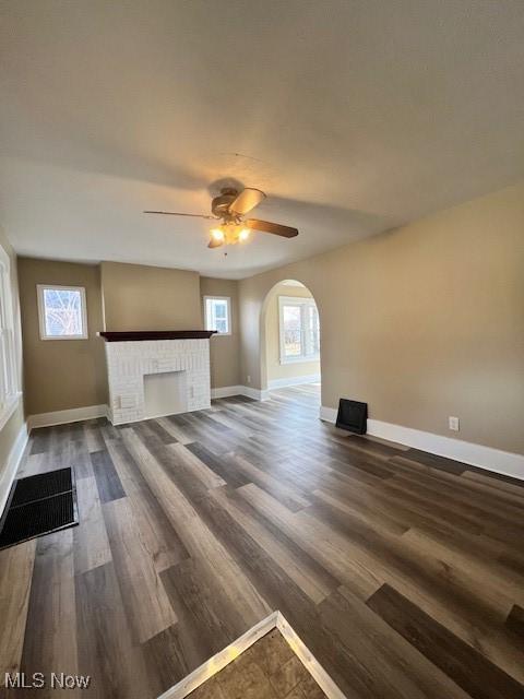 unfurnished living room featuring a fireplace, ceiling fan, and dark wood-type flooring