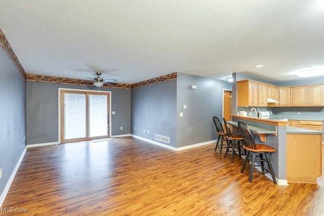 kitchen with kitchen peninsula, light brown cabinetry, light wood-type flooring, a breakfast bar, and ceiling fan